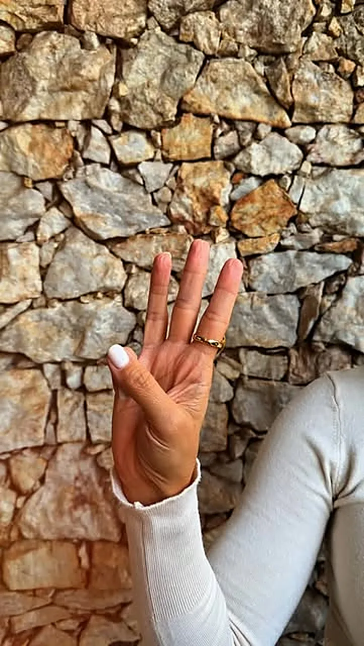 Mão fazendo sinal de ok diante de um muro de pedra